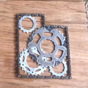 Puede incluir: Una pieza de arte de pared de metal con forma del estado de Utah, hecha de una cadena y varios engranajes.