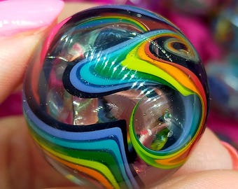 May include: A spherical glass marble featuring a clear exterior and an internal swirling pattern of vibrant rainbow colours including blue, green, yellow, orange, and purple. The design consists of layered, flowing bands of colour that create a dynamic, multi-dimensional effect within the transparent glass sphere.
