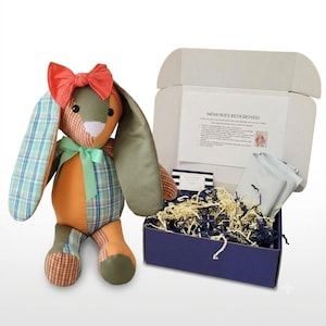 May include: A stuffed rabbit toy made from various fabric patches in orange, green, and blue plaid, featuring a coral bow on its head and a mint green ribbon around its neck. Next to it is an open blue shipping box containing paper filler.