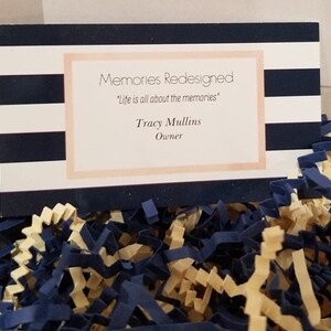 May include: A business card with a navy blue and white striped background. The text on the card reads "Memories Redesigned", "Life is all about the memories", "Tracy Mullins", and "Owner".