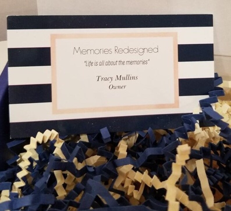 May include: A business card with a navy blue and white striped background. The text on the card reads "Memories Redesigned", "Life is all about the memories", "Tracy Mullins", and "Owner".