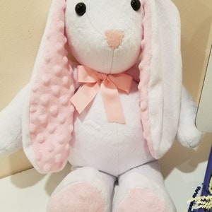 May include: A white plush bunny with pink ears and feet. The bunny has a pink bow around its neck.
