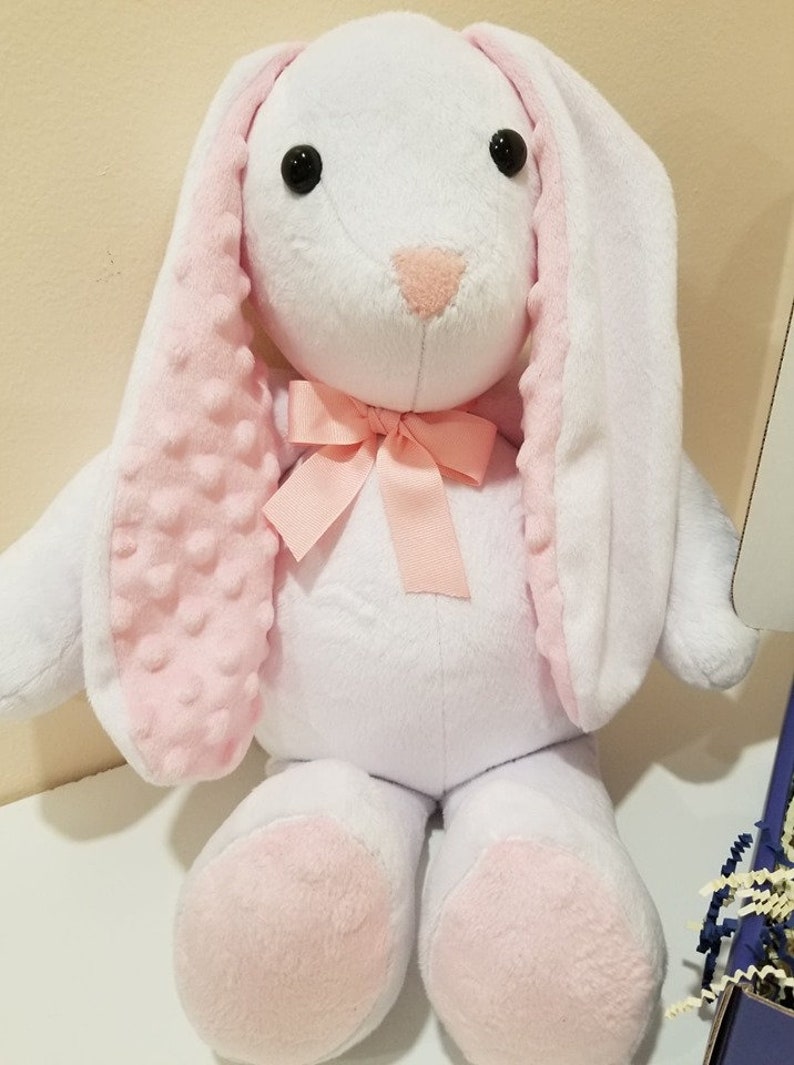 May include: A white plush bunny with pink ears and feet. The bunny has a pink bow around its neck.