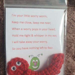 Puede incluir: Un gusano de la preocupación de crochet rojo con ojos saltones y un poema que dice: "Soy tu pequeño gusano de la preocupación, Mantenme cerca, mantenme cerca, Cuando una preocupación te llega a la cabeza, Abrázame fuerte y susúrrame al oído, Te quitaré tu preocupación, Así que no tendrás nada que temer."