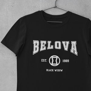 Puede incluir: Camiseta negra con texto blanco que dice "BELOVA EST. 1989 BLACK WIDOW" con un símbolo de viuda negra en un círculo.