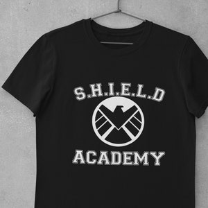 May include: Black t-shirt with a white graphic of the S.H.I.E.L.D. logo and the text "S.H.I.E.L.D. ACADEMY".