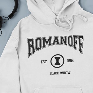 May include: White hooded sweatshirt with the text "ROMANOFF" in black, with a black widow symbol and the text "EST. 1984 BLACK WIDOW" underneath.