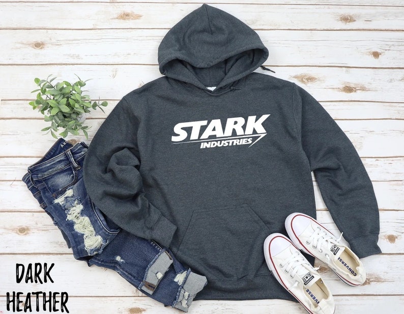 May include: Dark heather grey hoodie with a white graphic of the Stark Industries logo. The logo features the word "Stark" in a bold white font with a white arrow pointing to the right. The words "Industries" are printed in a smaller white font below the word "Stark".