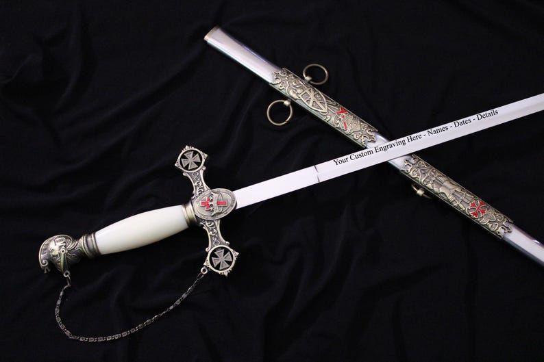 May include: A ceremonial sword with a white handle and a silver blade. The hilt features a cross design with red accents. The scabbard is silver with ornate detailing. Text on the blade reads "Your Custom Engraving Here - Names - Dates - Details."