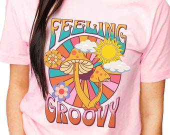 Könnte beinhalten: Pinkes T-Shirt mit einer Retro-Grafik von Pilzen, Blumen und einer Sonne mit dem Text "Feeling Groovy".