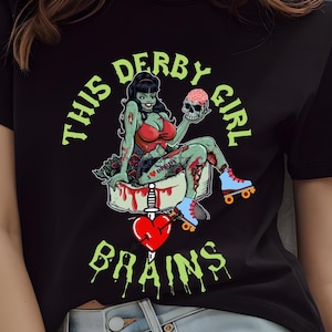 Könnte beinhalten: Schwarzes T-Shirt mit einem grünen Zombie-Roller-Derby-Girl-Motiv. Der Aufdruck lautet "This Derby Girl Brains" mit einem Herz und einem Dolch.