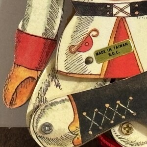 May include: A vintage wooden toy soldier with red, white, and black painted details. The soldier is wearing a black belt with a gold buckle and has a gold label that reads "Made in Taiwan R.O.C."