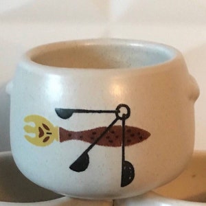 Peut inclure: Un ensemble de trois bols en céramique blanche avec un motif d'ustensiles de cuisine brun, jaune et noir. Les bols sont empilés les uns sur les autres.