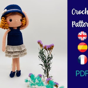 Puede incluir: Patrón de crochet para una muñeca con un vestido azul y un sombrero blanco. El patrón está disponible en inglés, español y francés. El patrón es una descarga PDF.