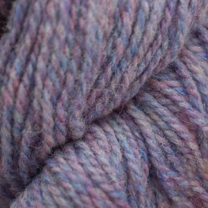 May include: Close-up of a skein of yarn in shades of purple, blue, and white. The yarn is soft and fluffy, with a slightly textured appearance.
