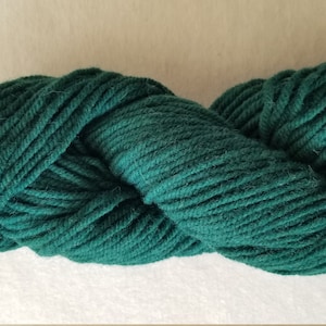 May include: A skein of dark green yarn, a deep forest green color. The yarn is made of wool and is soft and fluffy.