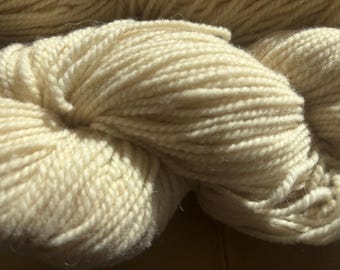 Puede incluir: Un primer plano de una madeja de hilo de color crema. El hilo es suave y esponjoso, y es perfecto para tejer o hacer ganchillo.