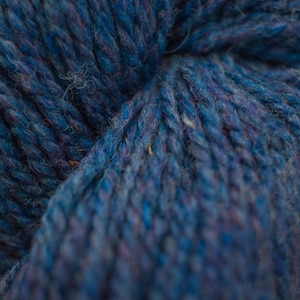May include: Close-up of a deep blue yarn with a subtle purple hue. The yarn is soft and textured, with a slightly fuzzy appearance.