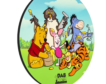 May include: A round, colorful coaster featuring Winnie the Pooh, Piglet, Eeyore, and Owl, all covered in honey. The coaster has a green background and the text "Dab Matz" in black.