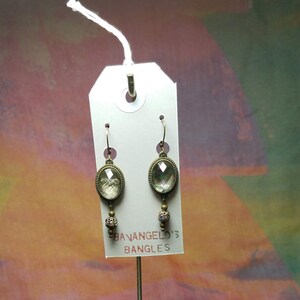 Könnte beinhalten: Ein Paar Ohrhänger mit ovalen, regenbogenfarbenen Glassteinen und kleinen, glitzernden Perlen. Die Ohrringe werden auf einer weißen Karte mit dem Text "BAVANGELO'S BANGLES" präsentiert.