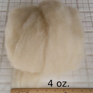 May include: A close-up of a 4 ounce pile of white wool roving. The wool is arranged in two rows and is sitting on a white gridded surface.