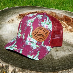 May include: A maroon trucker hat with a cactus print and a brown leather patch that says "Killin' It".