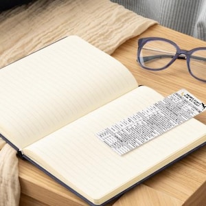 May include: A blue notebook with lined pages is open on a wooden table. A pair of eyeglasses and a small piece of paper with text are on the table. The paper has the text "Secret Code: How We Do This".