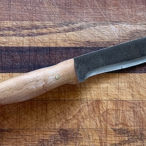 May include: A wooden handled knife with a black blade, resting on a wooden cutting board.