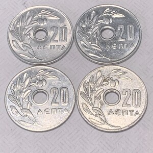 May include: Four silver Greek coins with a hole in the center. Each coin has a design of an olive branch and the text "20 ΛΕΠΤΑ".