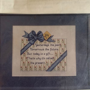May include: Cross stitch pattern with a blue ribbon and a yellow tag that says "Today". The text reads "Yesterday's the past, Tomorrow's the future. But today is a gift... That's why it's called the present."