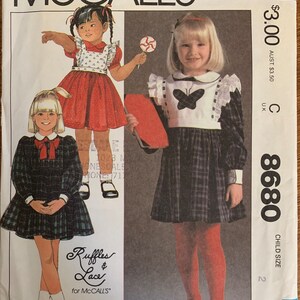 May include: A sewing pattern for a child's dress. The pattern is for a plaid dress with a white collar and a butterfly applique. The pattern is from McCall's and is size 2.