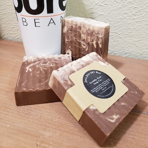 May include: Three bars of brown and white marbled soap with a brown paper label that reads "Java Jive 605 Bar Grabby Goat Soap Co.".