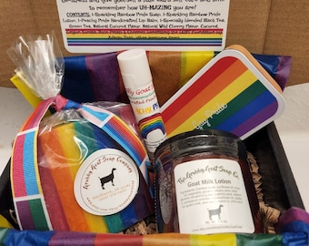 May include: A rainbow-themed gift box filled with bath and body products. The box contains a rainbow-striped soap, a rainbow-striped lotion, a lip balm, and a jar of goat milk lotion. The box is decorated with a rainbow ribbon and a card that says "Celebrating You!"