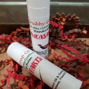 May include: Two lip balm tubes, one white with the text "Grubby GoatSoap" and "Lip Balm" and the other white with the text "FARTS" and "Coconut Oil & Cocoa Beeswax, Flavor 0".
