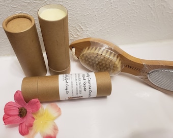 May include: Two brown cardboard tubes with white labels that read "HooF Repair Naturally Healing Foot Balm -  Made with 100% Caprine Grade -  Body Goat Soap Co.". One tube is open and contains a white balm. A wooden foot brush with a bristle brush on one end and a metal foot file on the other end. The brush is wrapped in plastic.