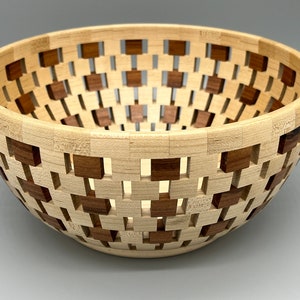 May include: A wooden bowl with a geometric pattern. The bowl is made of light and dark wood, creating a contrasting design. The bowl is round and has a wide opening.