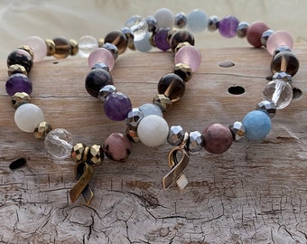 May include: Two bracelets with a variety of gemstone beads, including amethyst, rose quartz, aquamarine, and hematite. Each bracelet has a gold ribbon charm.