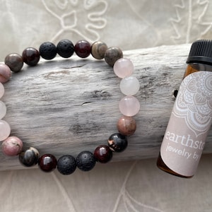 May include: A bracelet made with pink, black, and brown beads, along with a small bottle of essential oil. The bottle has a label that says "earthstone jewelry by".