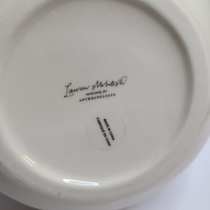 Puede incluir: Un plato de cer&aacute;mica blanco con el texto "Lauren McIntosh exclusivamente para ANTHROPOLOGIE" en escritura negra. Una peque&ntilde;a pegatina dice "MADE IN CHINA FABRIQUE EN CHINE".