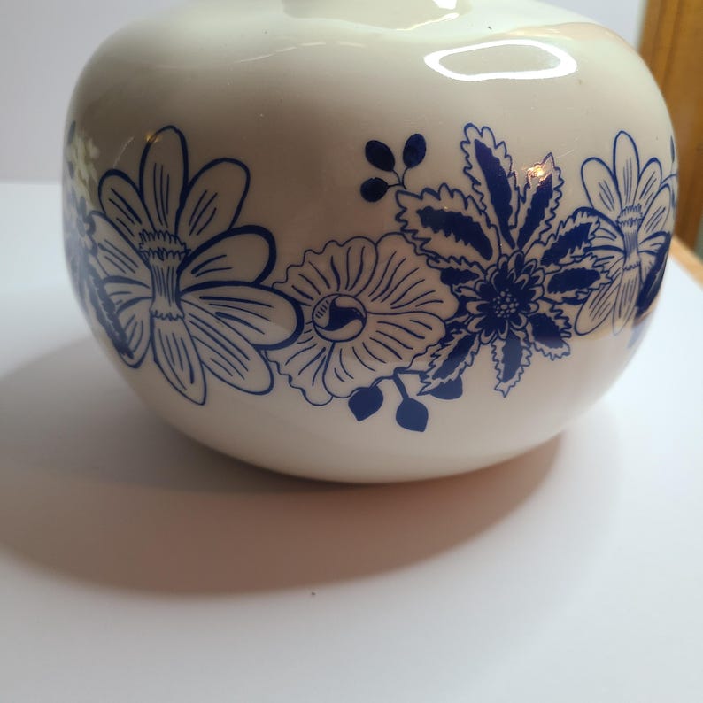 Puede incluir: Un jarr&oacute;n de cer&aacute;mica color crema con forma redondeada. El jarr&oacute;n est&aacute; decorado con un patr&oacute;n repetido de dise&ntilde;os florales azules. Las flores incluyen p&eacute;talos y hojas detallados, creando un aspecto cl&aacute;sico y elegante.