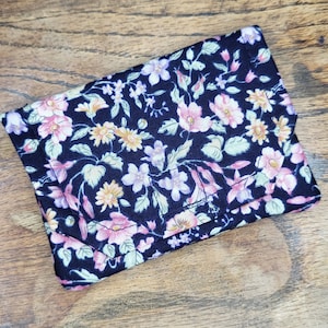May include: A small black fabric wallet with a floral print featuring pink, purple, and yellow flowers. The wallet is folded closed.