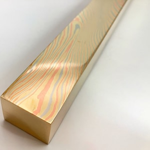 May include: A long, rectangular block of wood with a colorful, marbled pattern in shades of pink, blue, and yellow. The wood is polished and has a smooth, glossy finish.