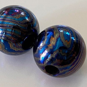 May include: Two round, blue, iridescent, metal beads with a hole through the centre. The beads have a swirling, marbled pattern in shades of blue, purple, and gold.