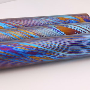 May include: Three cylindrical metal rods with a blue, purple, and gold iridescent finish. The rods have a wavy pattern.