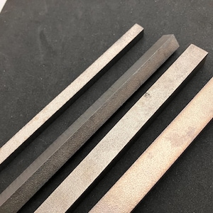 May include: Four metal files of varying shapes and textures are arranged diagonally against a dark background. The files appear to be made of steel, with a silver-gray color. The files are used for shaping and smoothing materials.