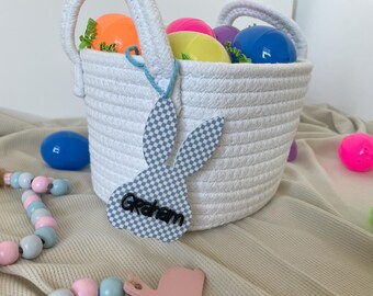 May include: White rope basket filled with colorful plastic Easter eggs. A blue and white bunny-shaped tag with the name "Graham" is attached to the basket.