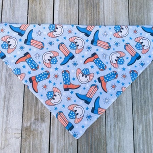Może przedstawiać: Niebieska bandana z wzorem czerwonych, białych i niebieskich kowbojskich but&oacute;w i uśmiechniętych twarzy w kowbojskich kapeluszach. Bandana leży na drewnianej powierzchni.
