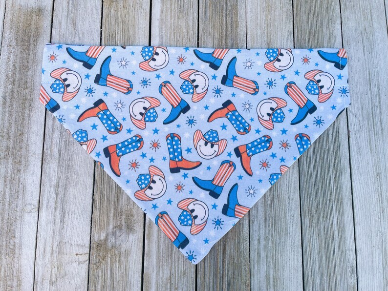 Może przedstawiać: Niebieska bandana z wzorem czerwonych, białych i niebieskich kowbojskich but&oacute;w i uśmiechniętych twarzy w kowbojskich kapeluszach. Bandana leży na drewnianej powierzchni.
