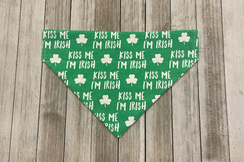 May include: Green dog bandana with white text and shamrock pattern. The text reads "KISS ME I'M IRISH" repeated across the fabric. The bandana is triangular in shape and made of fabric.