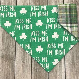 May include: Green dog bandana with white text that reads "Kiss Me I'm Irish" and shamrock graphics. The reverse side features a green, white, and yellow plaid pattern. A festive accessory for St. Patrick's Day.